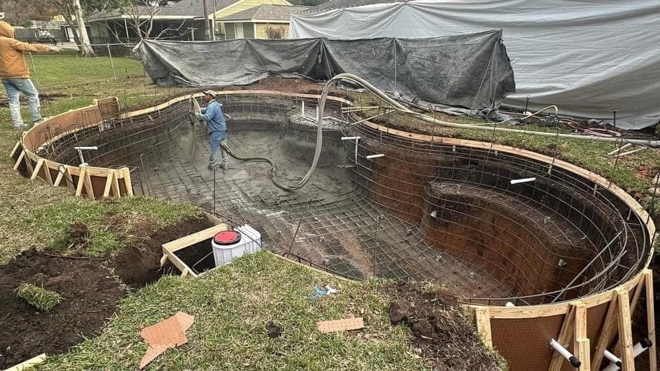 Worker spraying gunite on a freeform pool with rebar visible, residential backyard