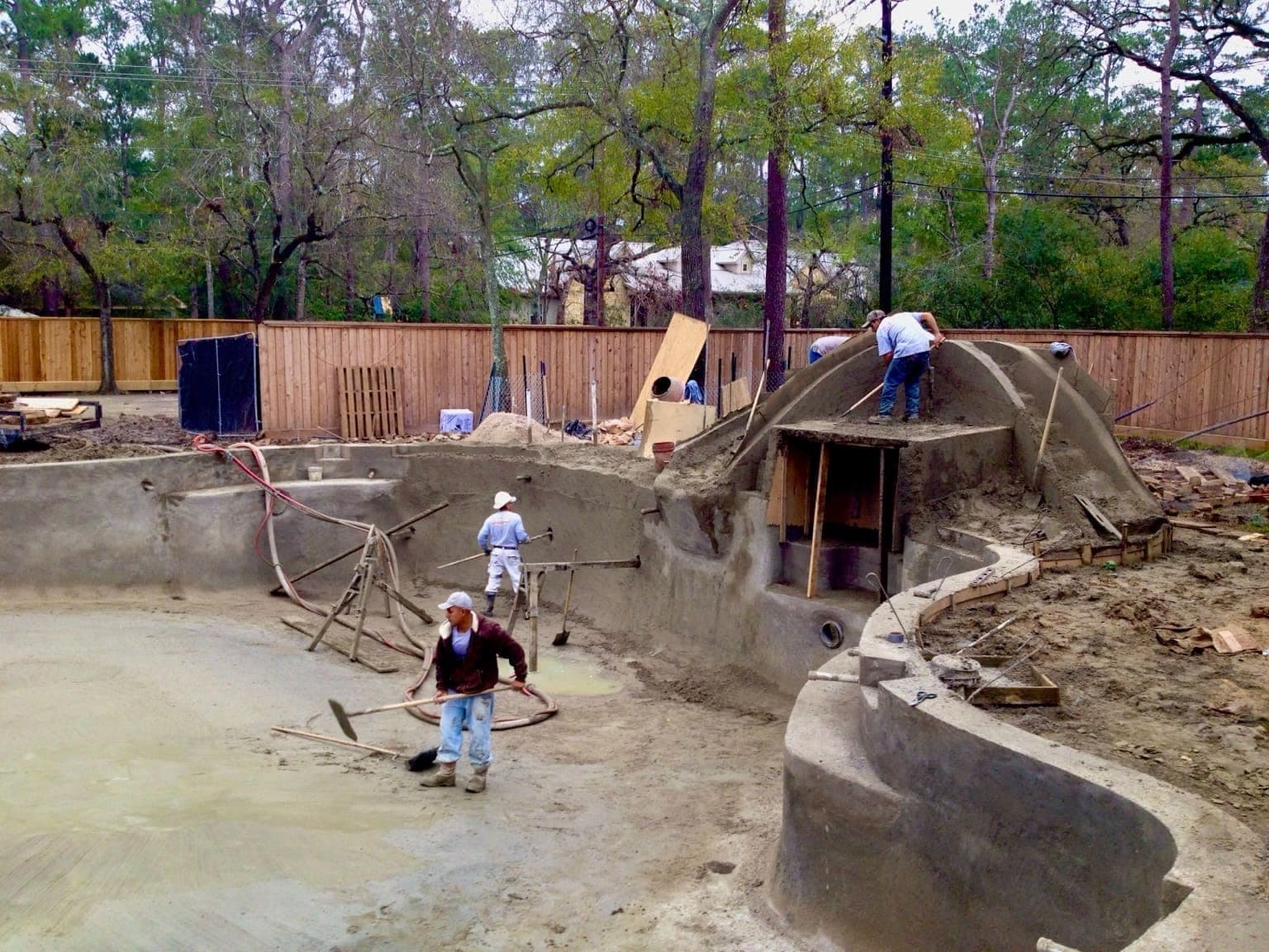Crew shotcreting a pool shell with a grotto arch form being shaped, complex curved design