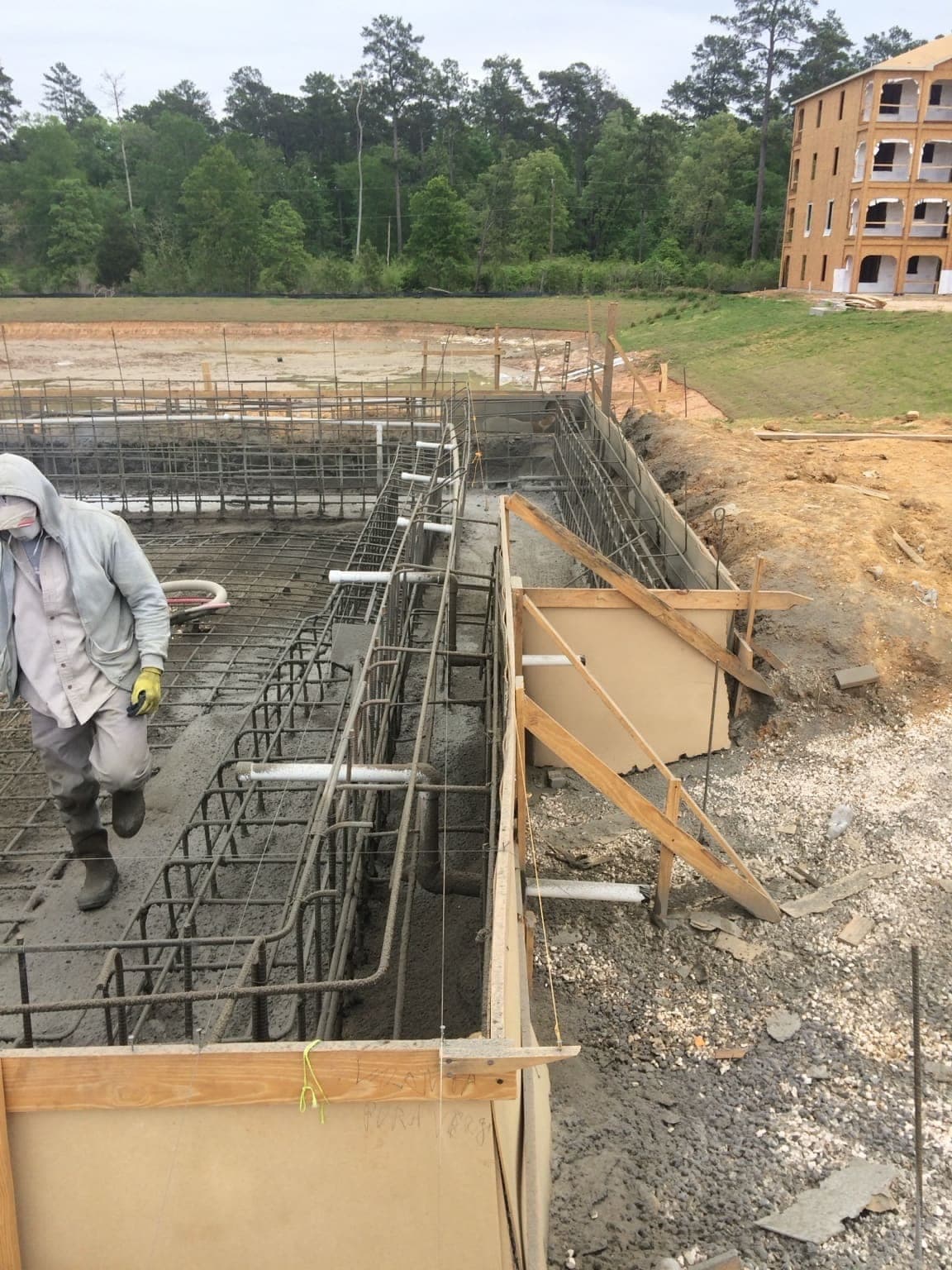 Commercial pool rebar cage and formwork from elevated angle, multi-story building in background