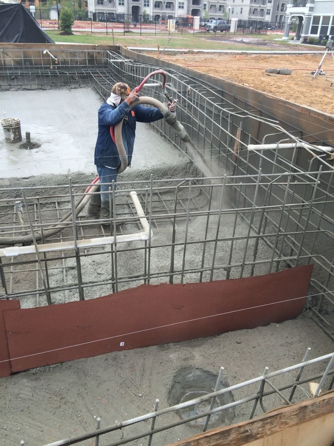 Nozzleman spraying shotcrete on commercial pool wall rebar, apartment complex jobsite